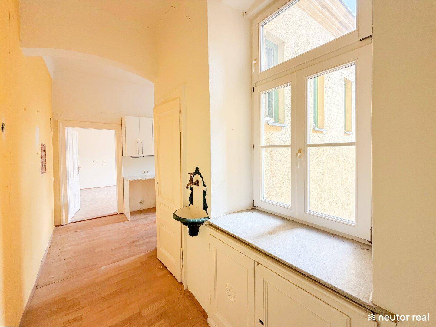 Heller Flur mit Holzboden, großem Fenster und einem kleinen Waschbecken an der Wand.