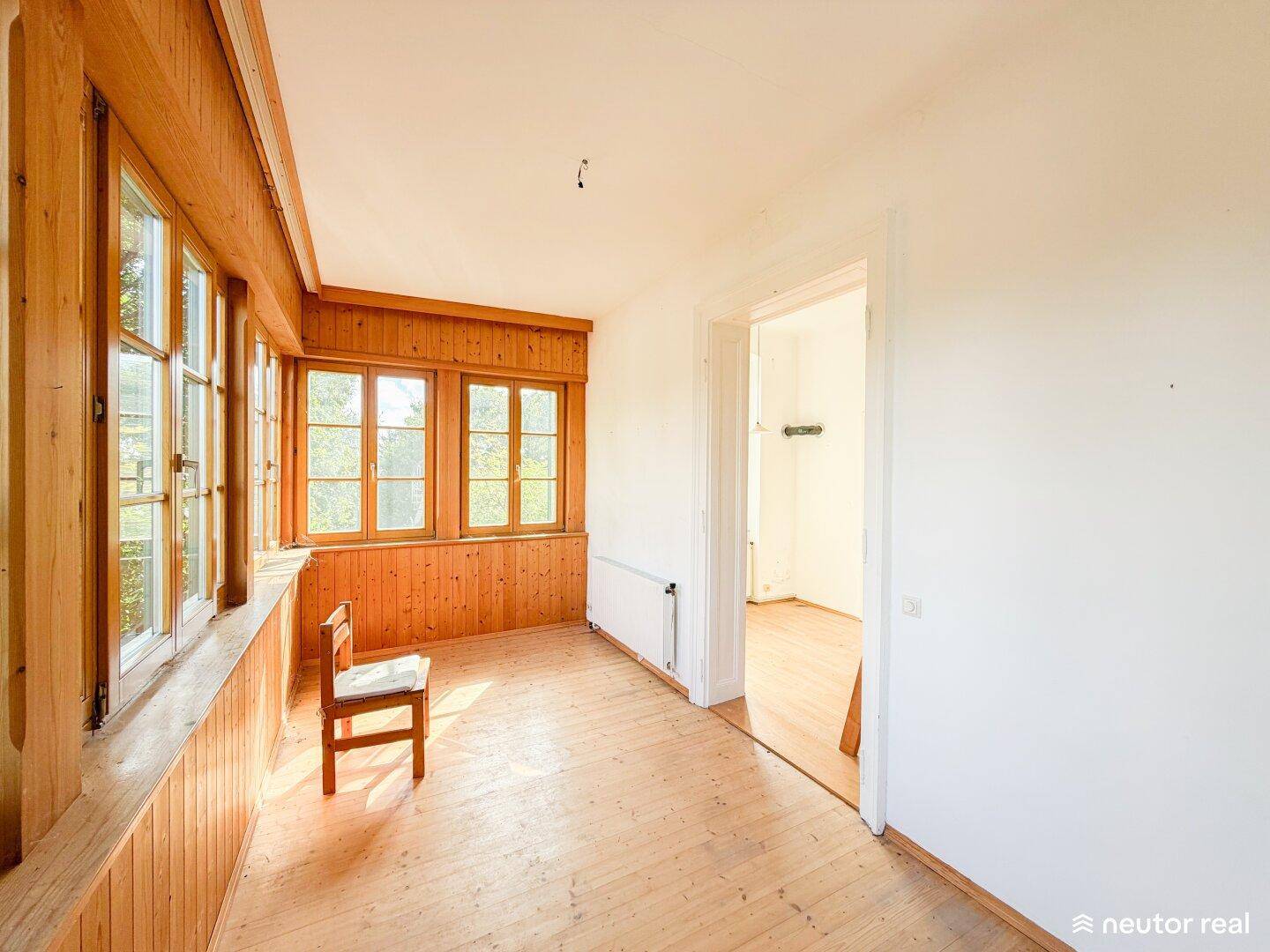 Lichtdurchfluteter Raum mit Holzboden und Holzverkleidung an Wänden und Decke, ideal als Wintergarten.