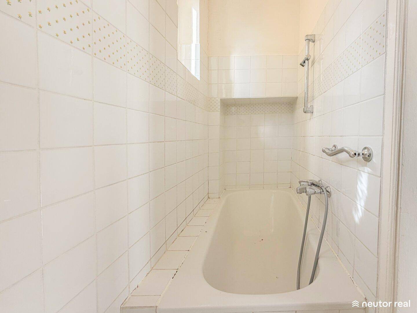 Badezimmer mit weiß gefliesten Wänden, Badewanne und Duscharmatur, in gutem Zustand.