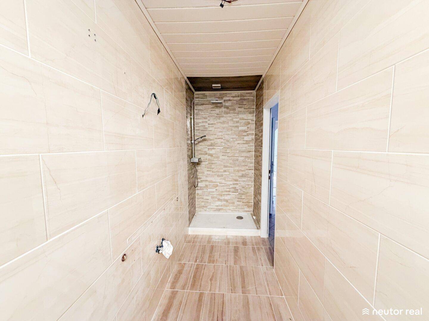 Modern gefliestes Badezimmer mit begehbarer Dusche und hellen Wand- und Bodenfliesen.