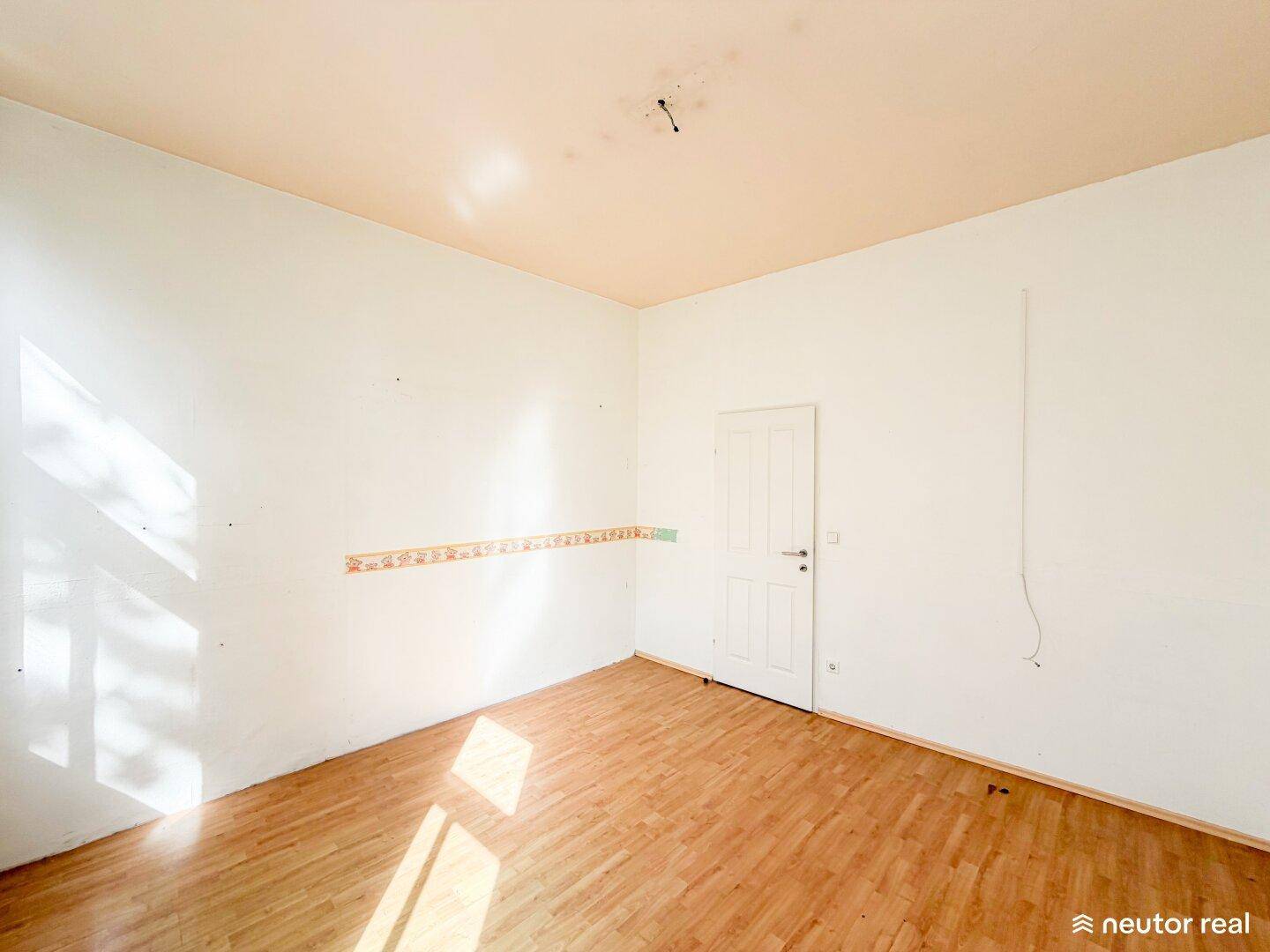 Schlafzimmer mit Laminatboden, weißen Wänden und einer Tür, bereit zur individuellen Gestaltung.