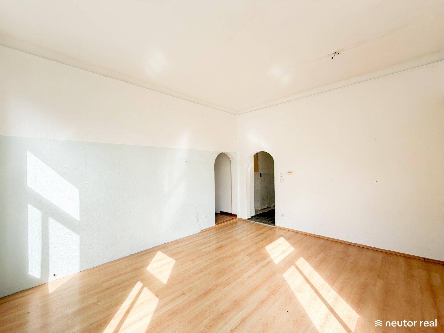 Helles Wohnzimmer mit Laminatboden und zwei eleganten Rundbögen, die zu weiteren Räumen führen.