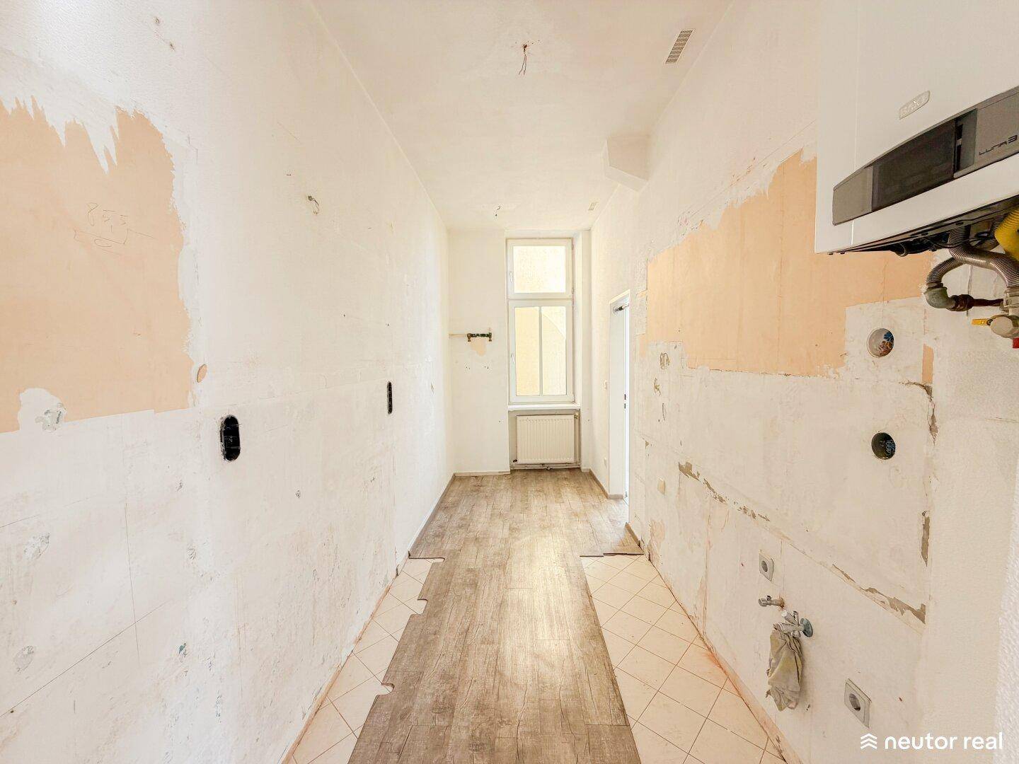Küche in Renovierung mit freigelegten Wänden, Fenster und Heizungsanlage, bereit für neue Einbauten.