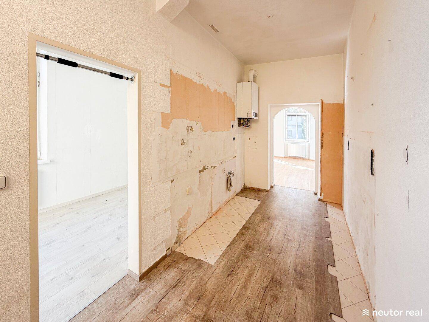 Renovierungsbedürftige Küche mit freigelegten Wänden, Heizungsanlage und Zugang zu angrenzenden Räumen.