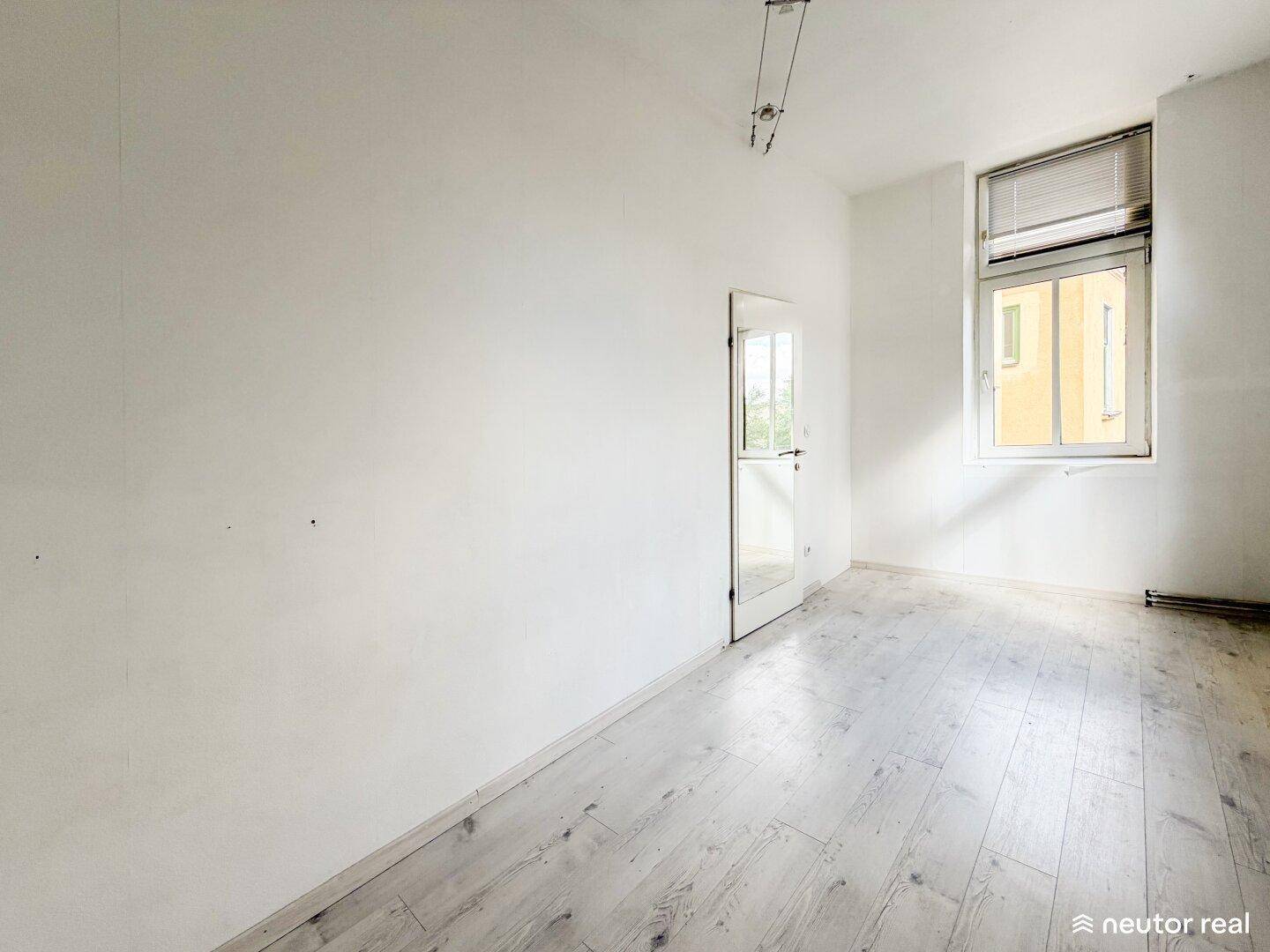 Schlafzimmer mit hellem Holzboden, weißen Wänden und einer Tür mit Glaseinsatz, in gutem Zustand.