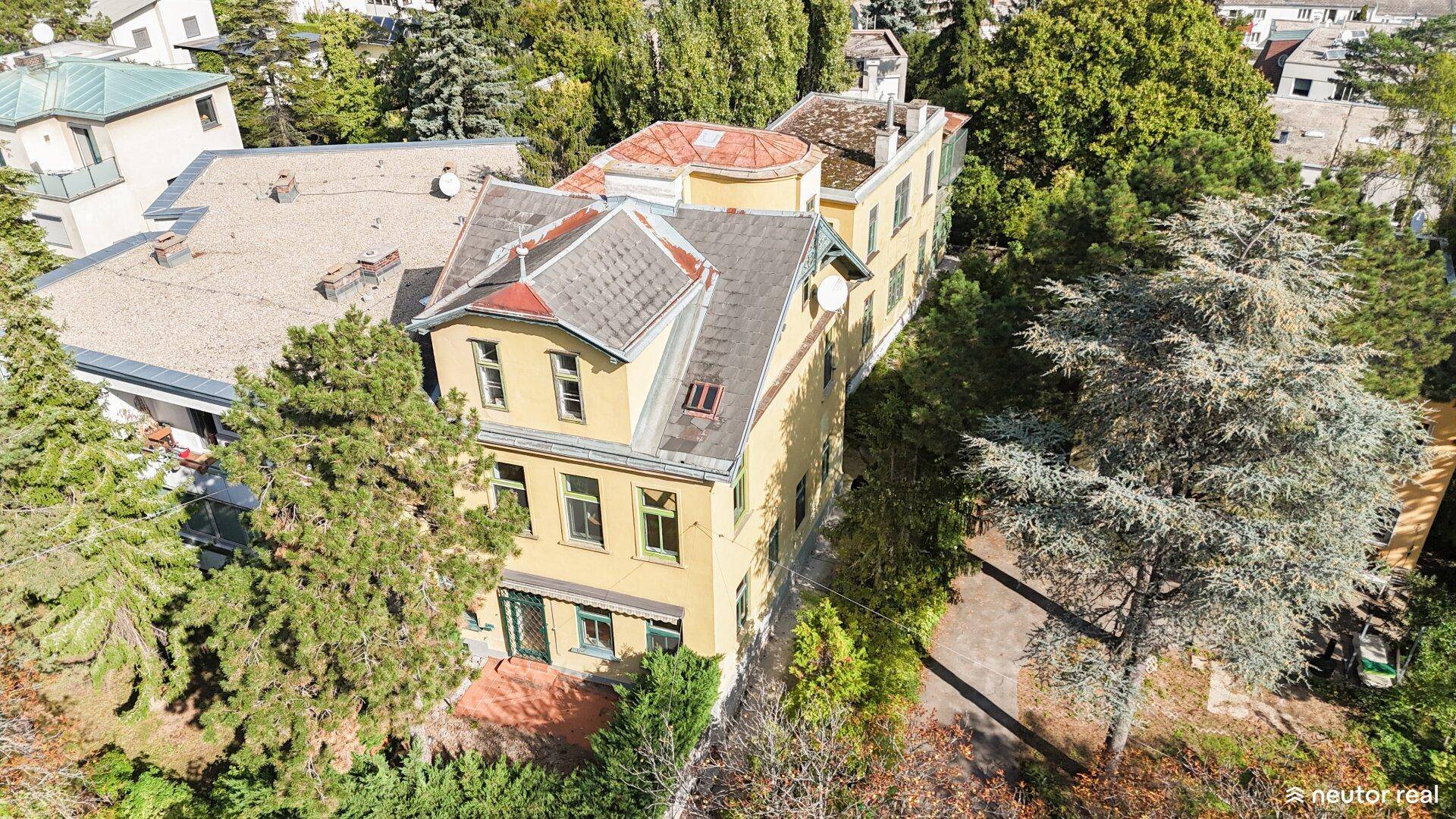 Luftaufnahme einer gelben Villa mit mehreren Dächern, umgeben von dichtem Baumbestand.