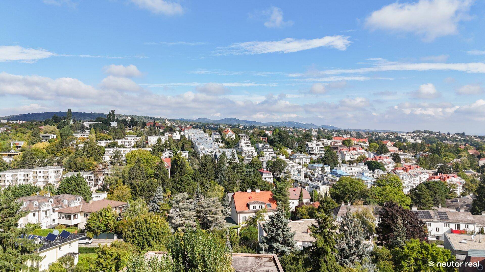 Weitläufiger Blick über die grüne Wohngegend mit vielen Häusern unter blauem Himmel.