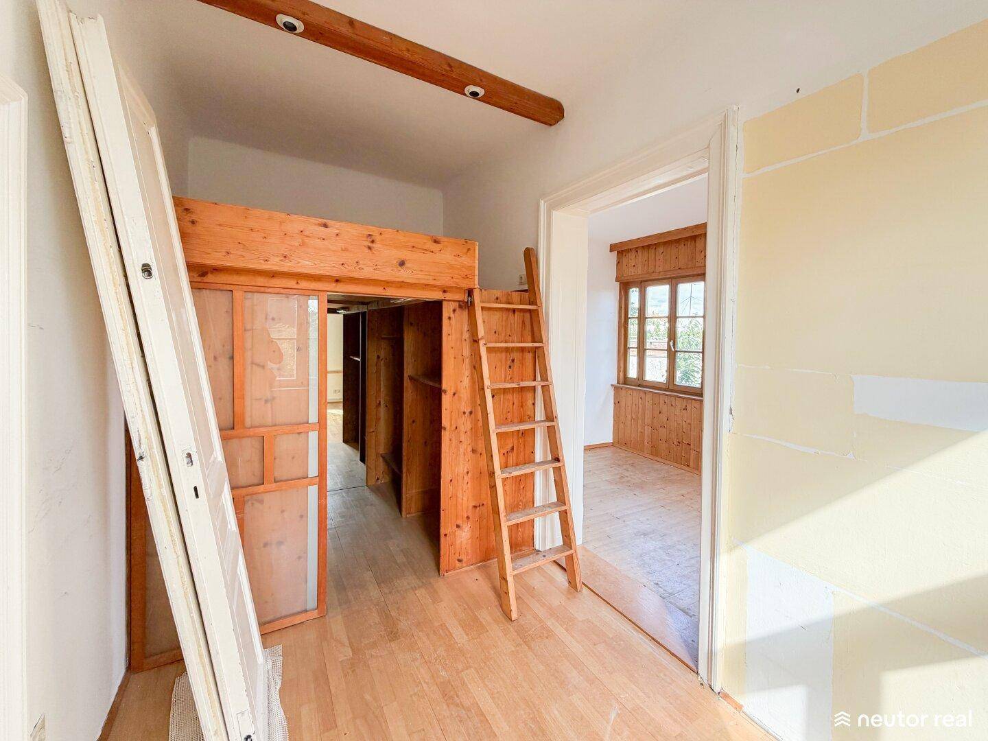 Zimmer mit Holzboden, Holz-Hochbettkonstruktion und Zugang zu einem weiteren Raum.