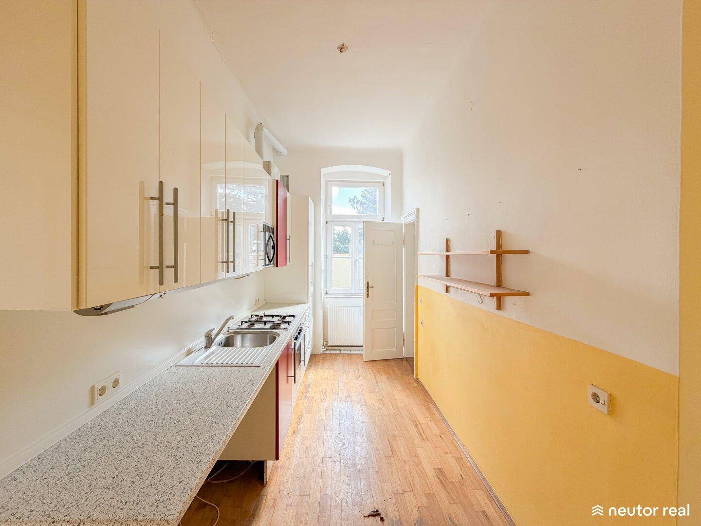 Helle Küche mit Gasherd, Spüle und Zugang zu einem kleinen Balkon.