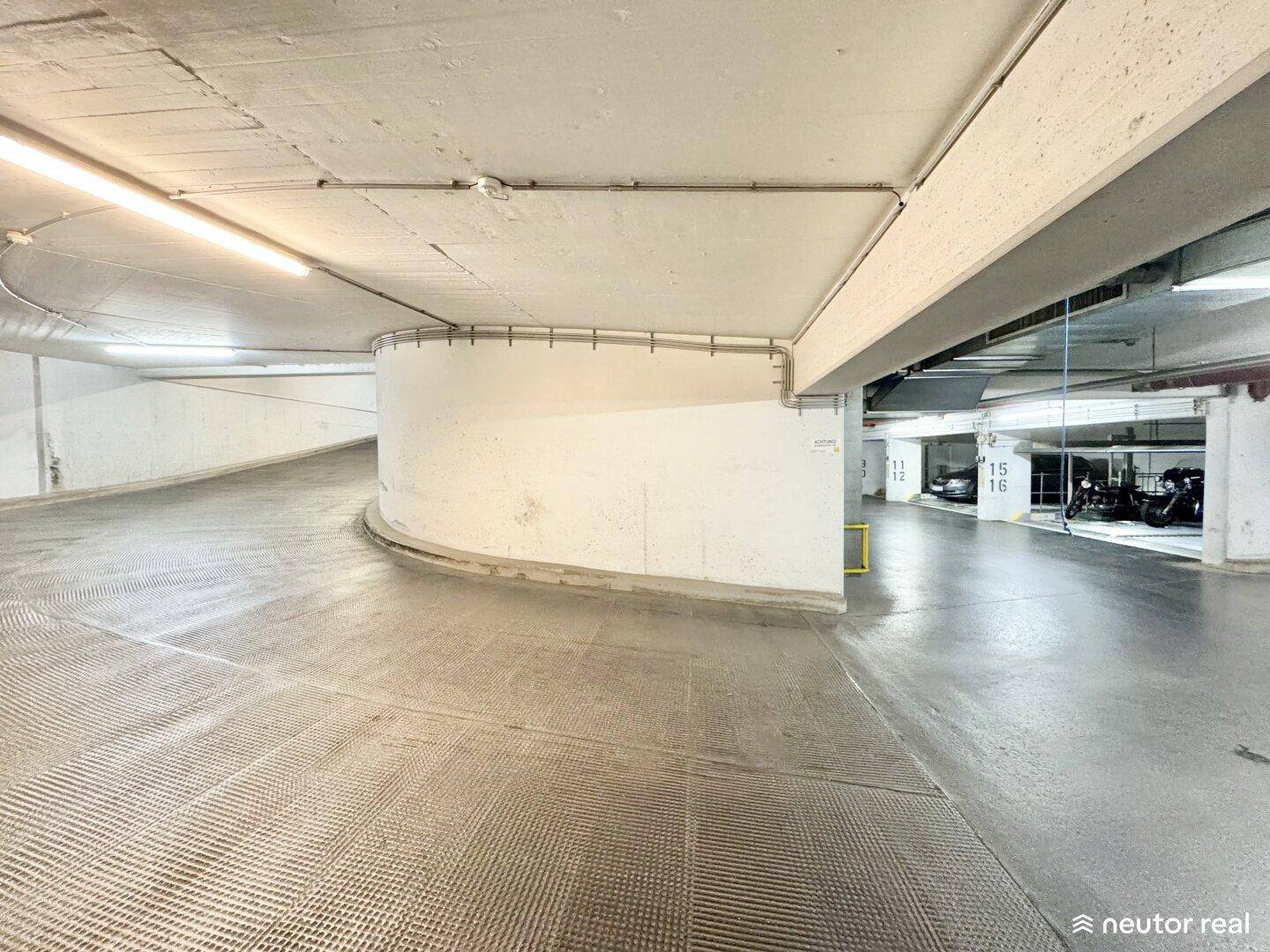 Kurvenreiche Rampe in einer Tiefgarage, die zu weiteren Parkebenen führt, mit Betonboden.