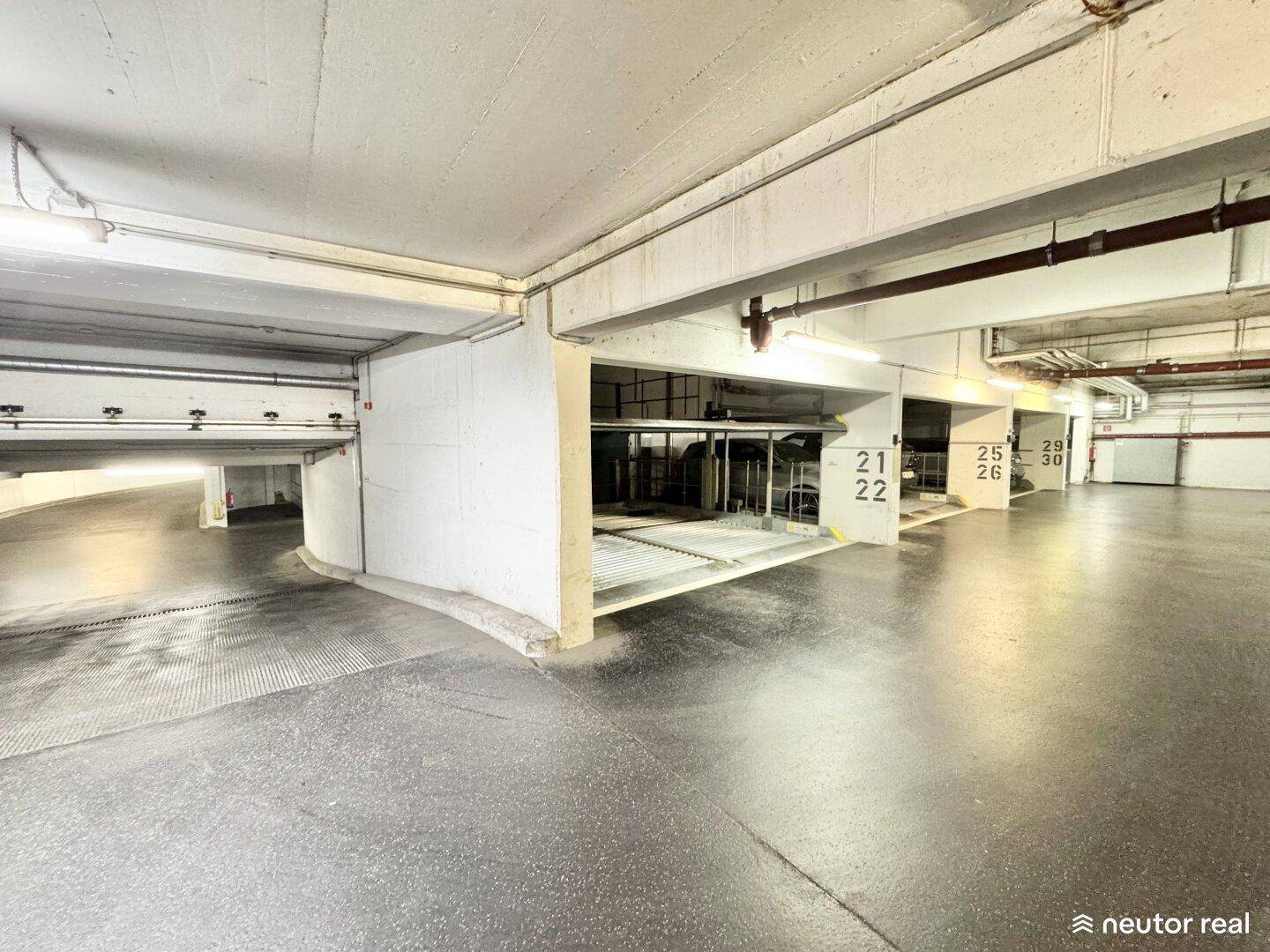 Geräumige Tiefgarage mit mehreren Parkplätzen und Zugang zu einer weiteren Parkebene.