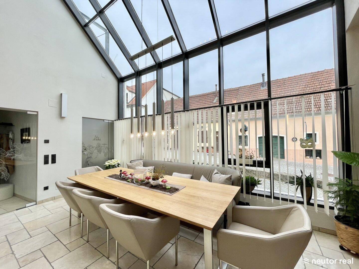 Heller Essbereich mit großem Holztisch, modernen Stühlen und beeindruckender Glasfront mit Blick nach draußen.