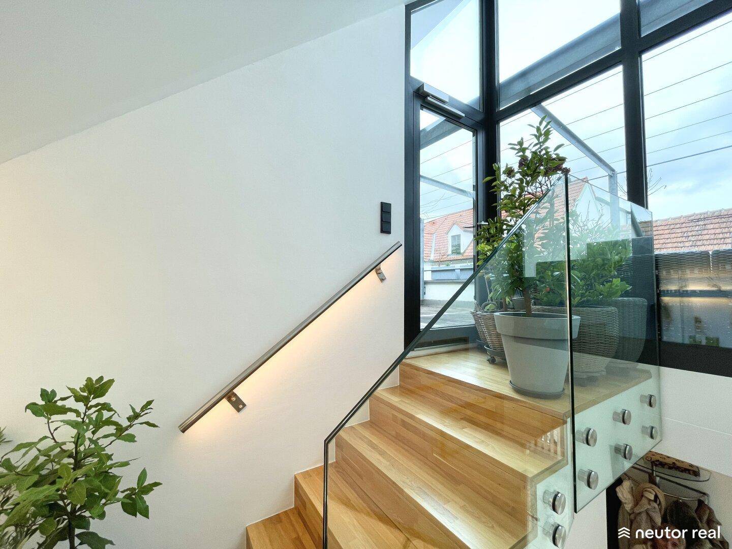 Holztreppe mit Glasgeländer und Handlauf, bietet einen Blick auf die beeindruckende Glasfassade.