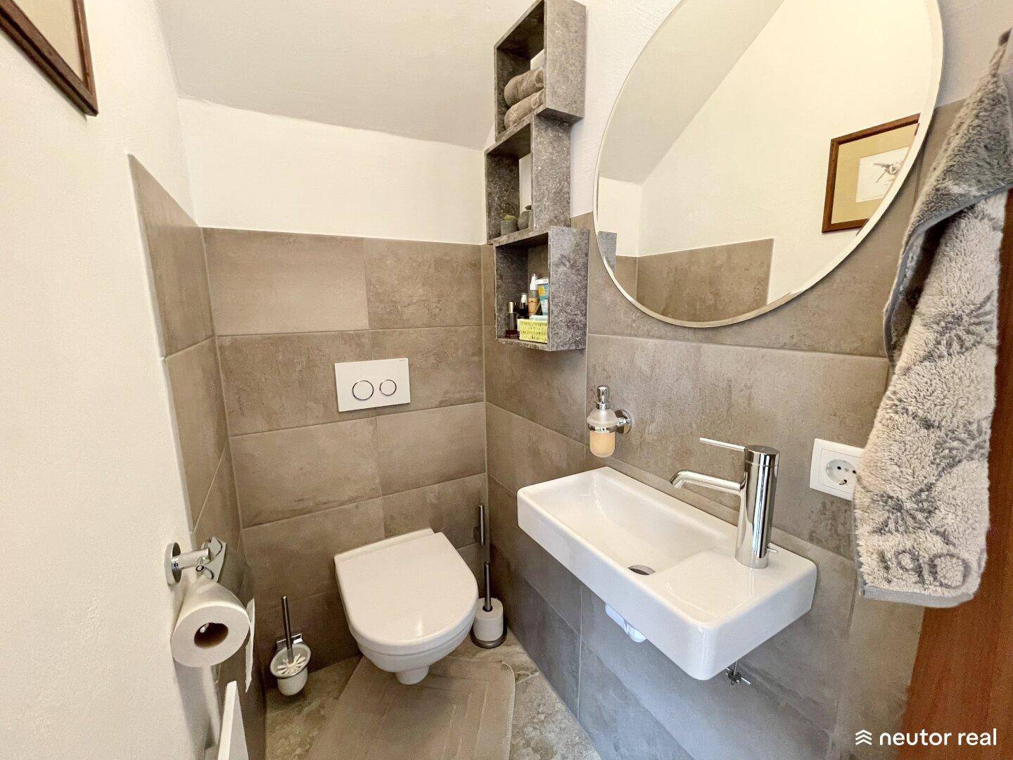 Modernes Gäste-WC mit wandhängender Toilette, kleinem Waschbecken und rundem Spiegel.