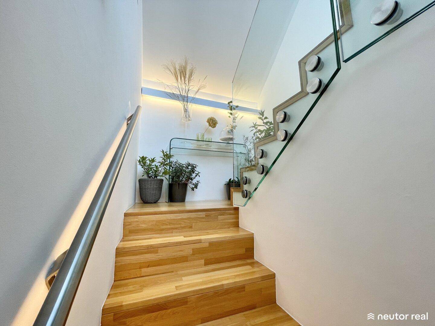 Elegante Holztreppe mit modernem Glasgeländer und indirekter Beleuchtung, führt in die oberen Etagen.