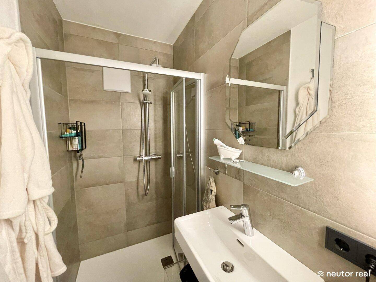 Kleines Badezimmer mit Duschkabine, modernem Waschbecken und beigefarbenen Wand- und Bodenfliesen.