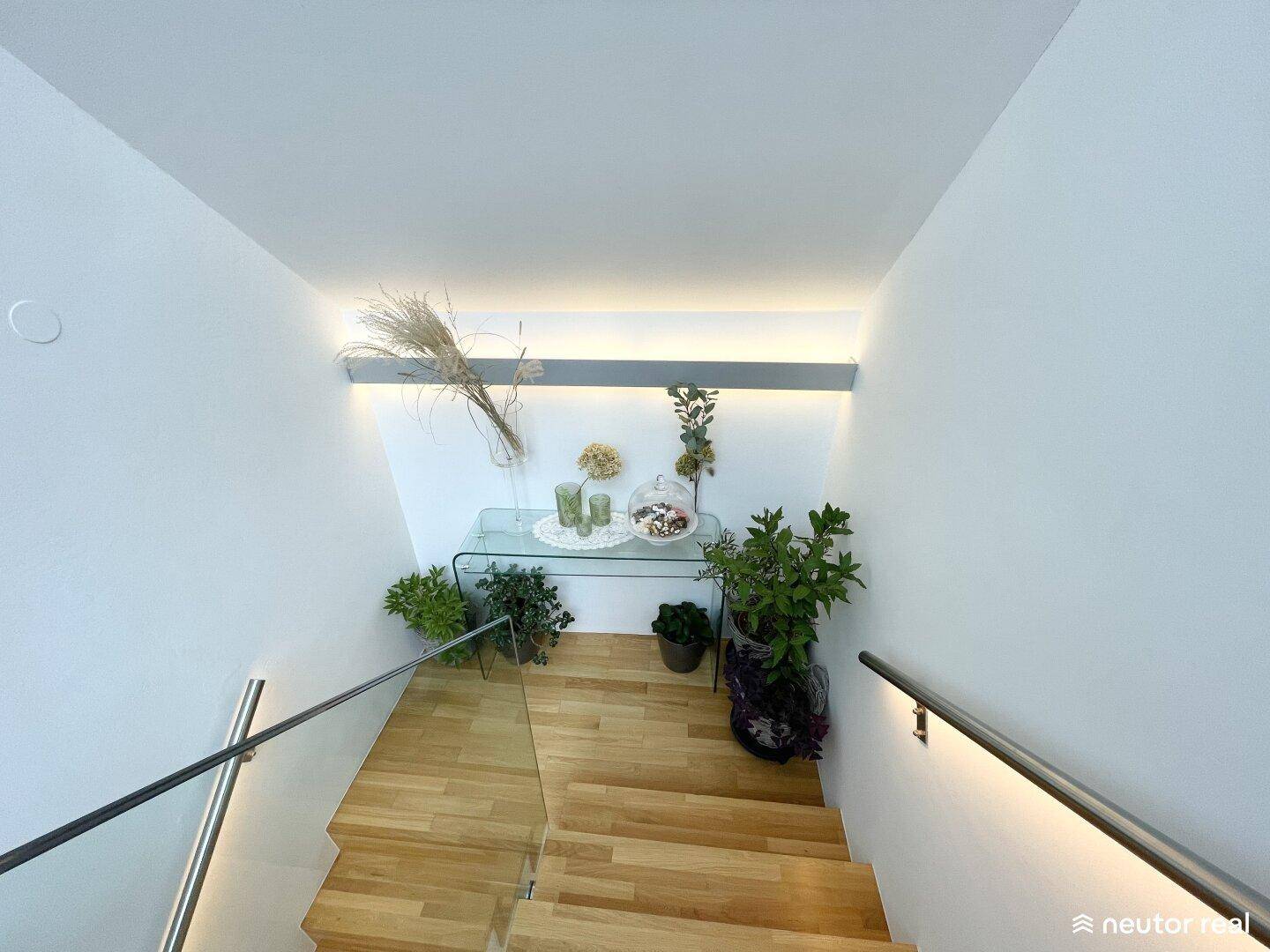 Moderne Holztreppe mit Glasgeländer und indirekter Beleuchtung, die zu den oberen Etagen führt.