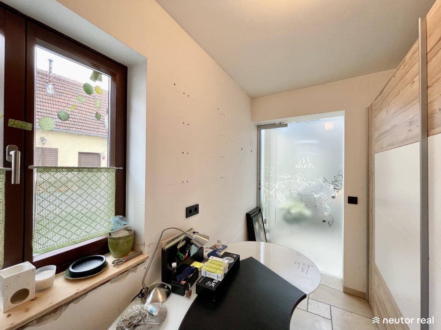 Kleiner Raum, möglicherweise ein Büro, mit Fenster und einer Milchglastür, die Licht hereinlässt.