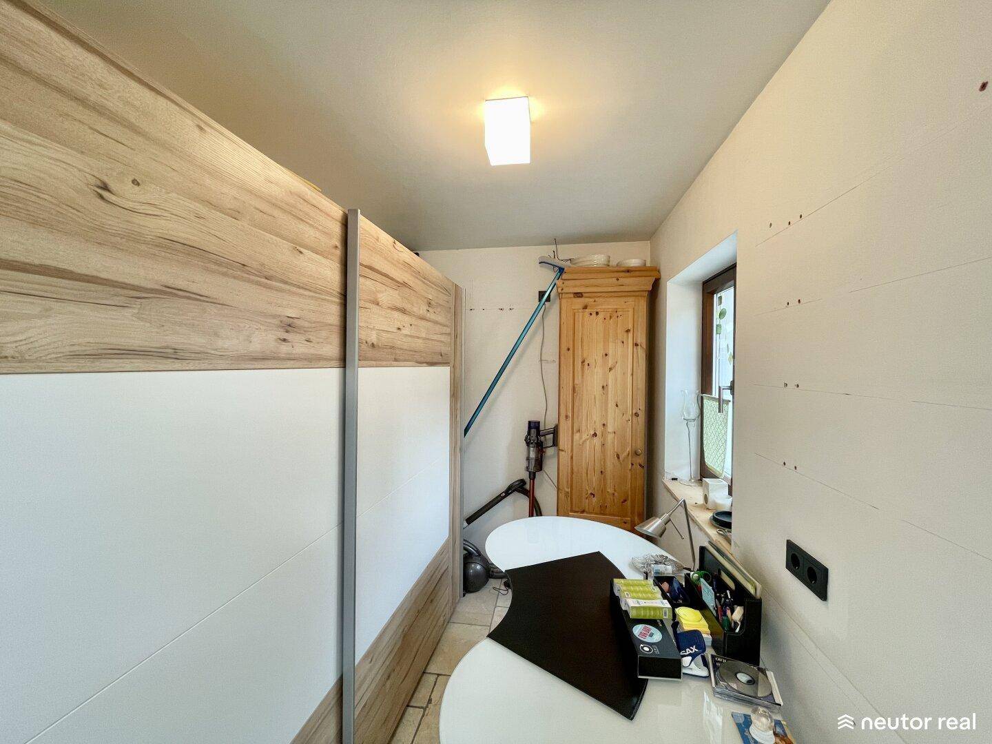 Ansicht des Raumes mit einem Holzschrank und einem Fenster, das Tageslicht hereinlässt.
