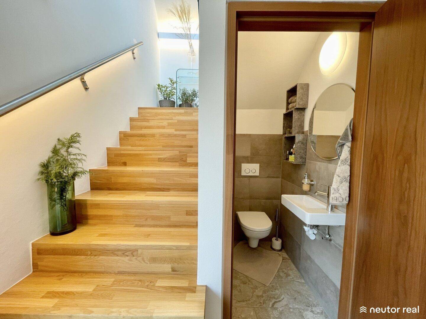Modernes Gäste-WC mit Wand-WC und Waschbecken, neben einer eleganten Holztreppe.