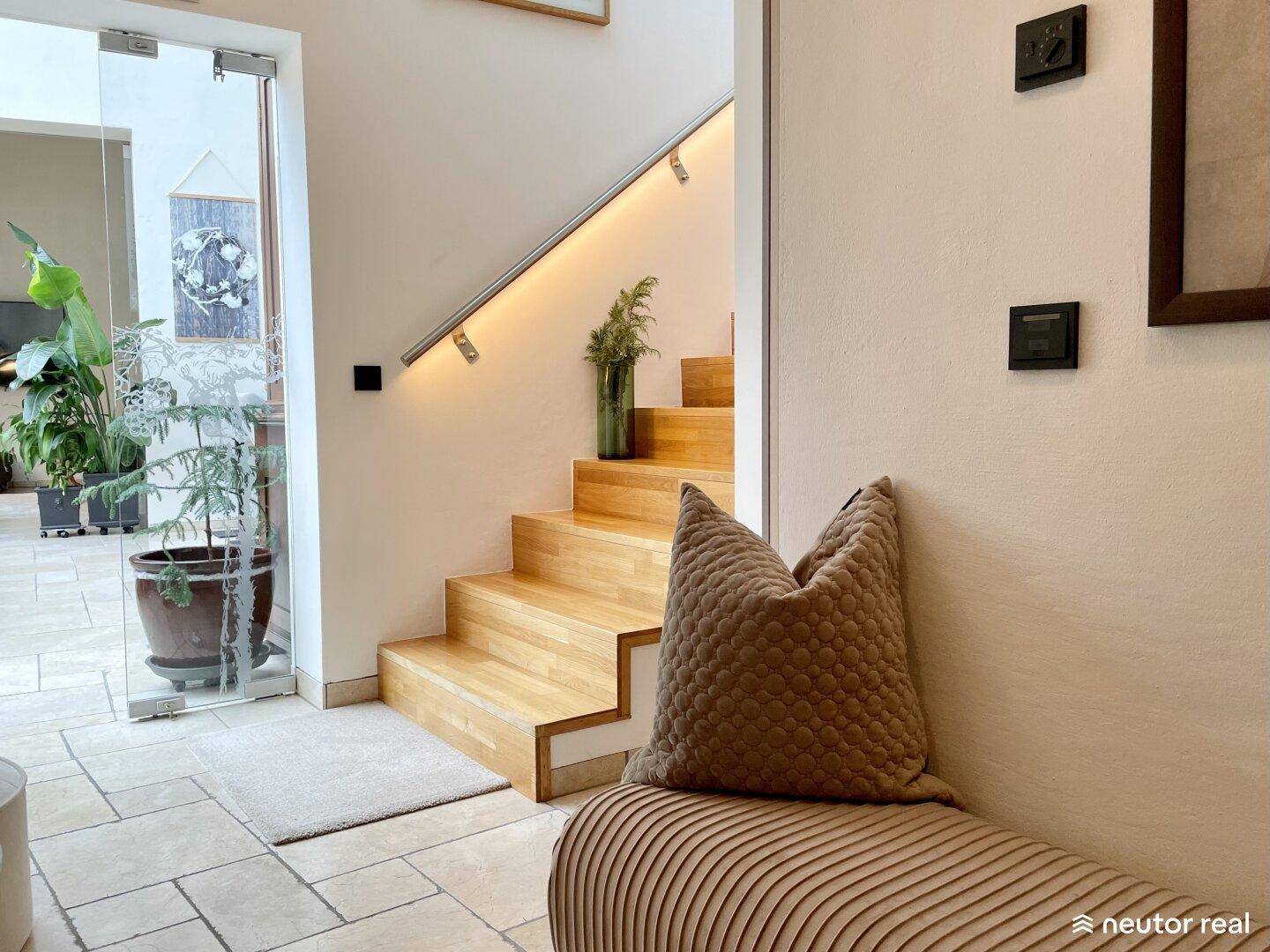 Detailansicht des Eingangsbereichs mit Holztreppe, beleuchtetem Handlauf und Steinfliesenboden.