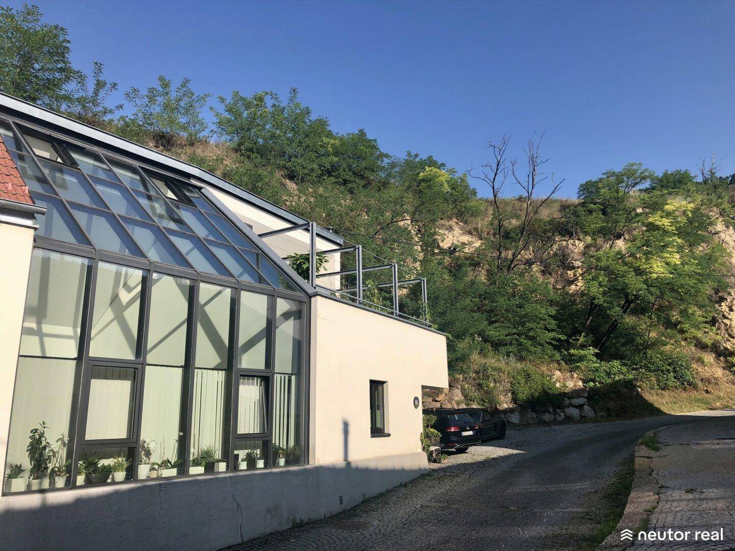 Die moderne Glasfassade des Hauses fügt sich in die natürliche Hanglage mit üppiger Vegetation ein.