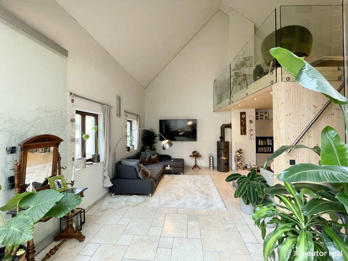 Gemütliches Wohnzimmer mit Sofa, Fernseher und einem Kaminofen, offen zur Galerie mit Glasgeländer.