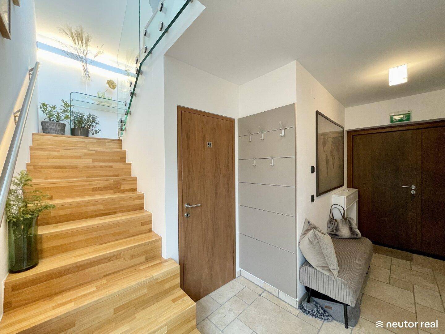 Heller Eingangsbereich mit moderner Holztreppe, Glasgeländer und Garderobe.