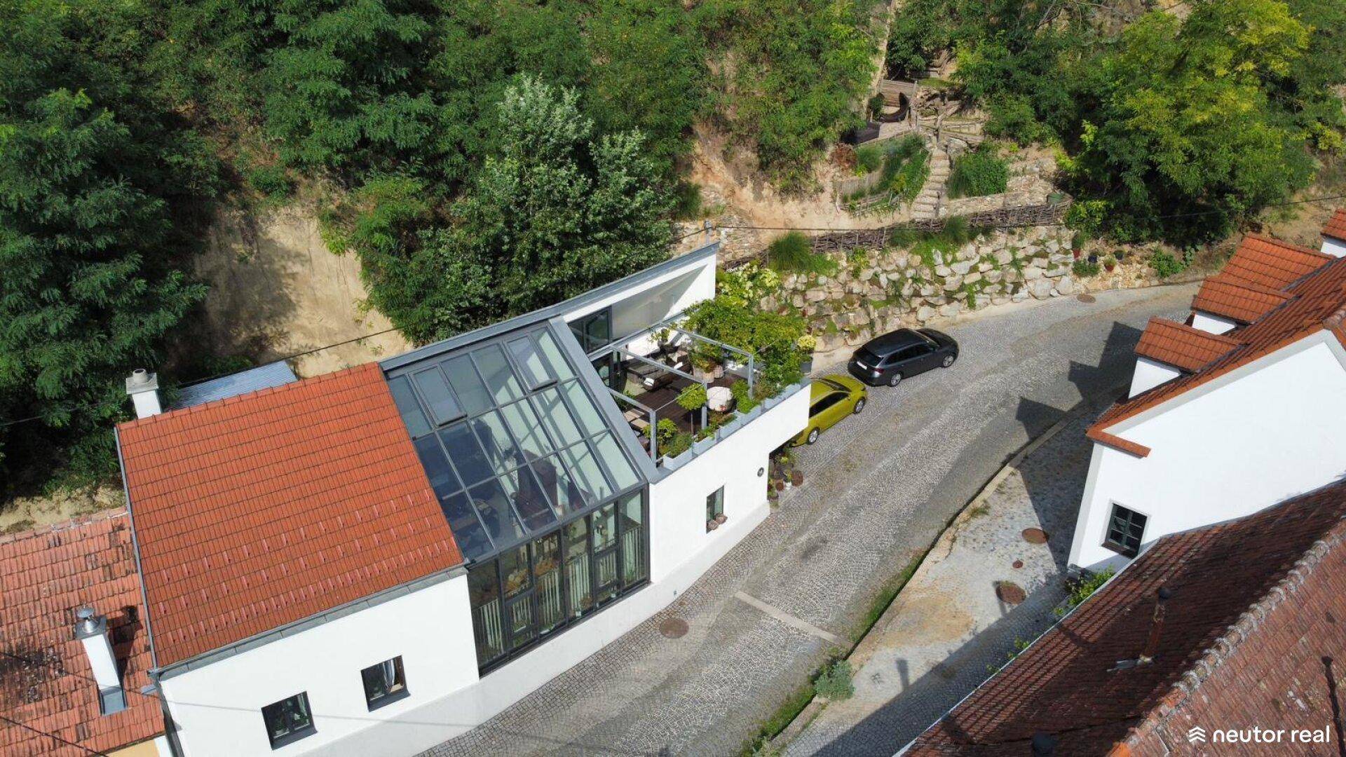 Dachterrasse eines modernen Hauses mit Glasdach und Blick auf die umliegende Straße und Natur.