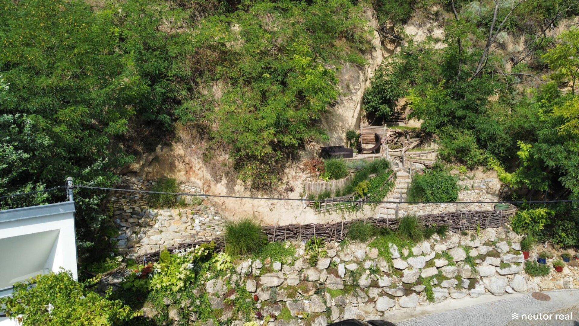 Terrassierter Garten an einem Hang mit Steinmauern und Treppen, umgeben von üppigem Grün.