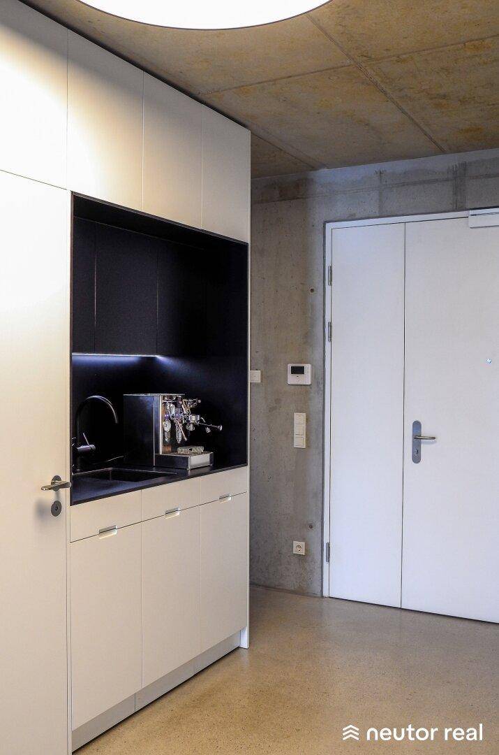 Moderne Teeküche mit weißen Schränken, integrierter Kaffeemaschine und minimalistischem Design.