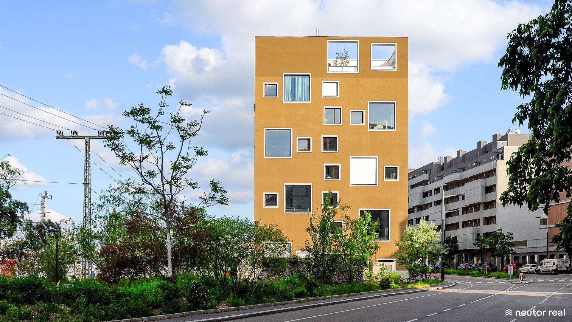 Modernes Gebäude mit auffälliger gelber Fassade und unregelmäßig angeordneten Fenstern in urbaner Umgebung.