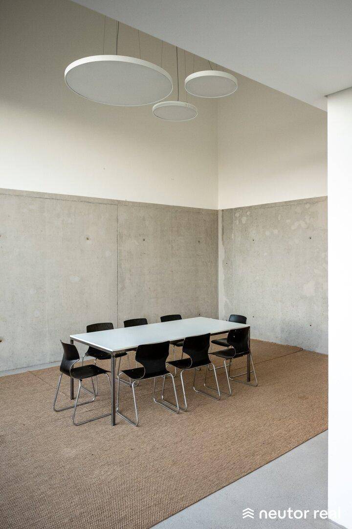 Geräumiger Besprechungsraum mit großem Tisch, modernen Pendelleuchten und einem Teppichboden.