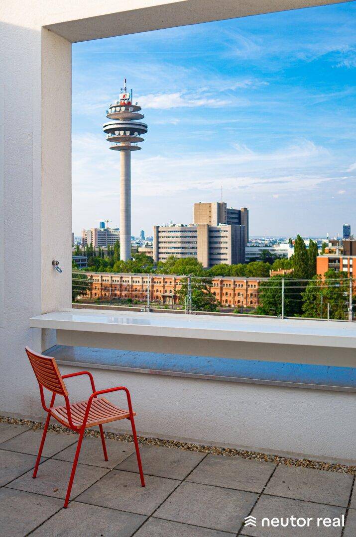 Sonniger Terrassenbereich mit orangefarbenem Stuhl und weitem Blick über die Stadt mit Fernsehturm.