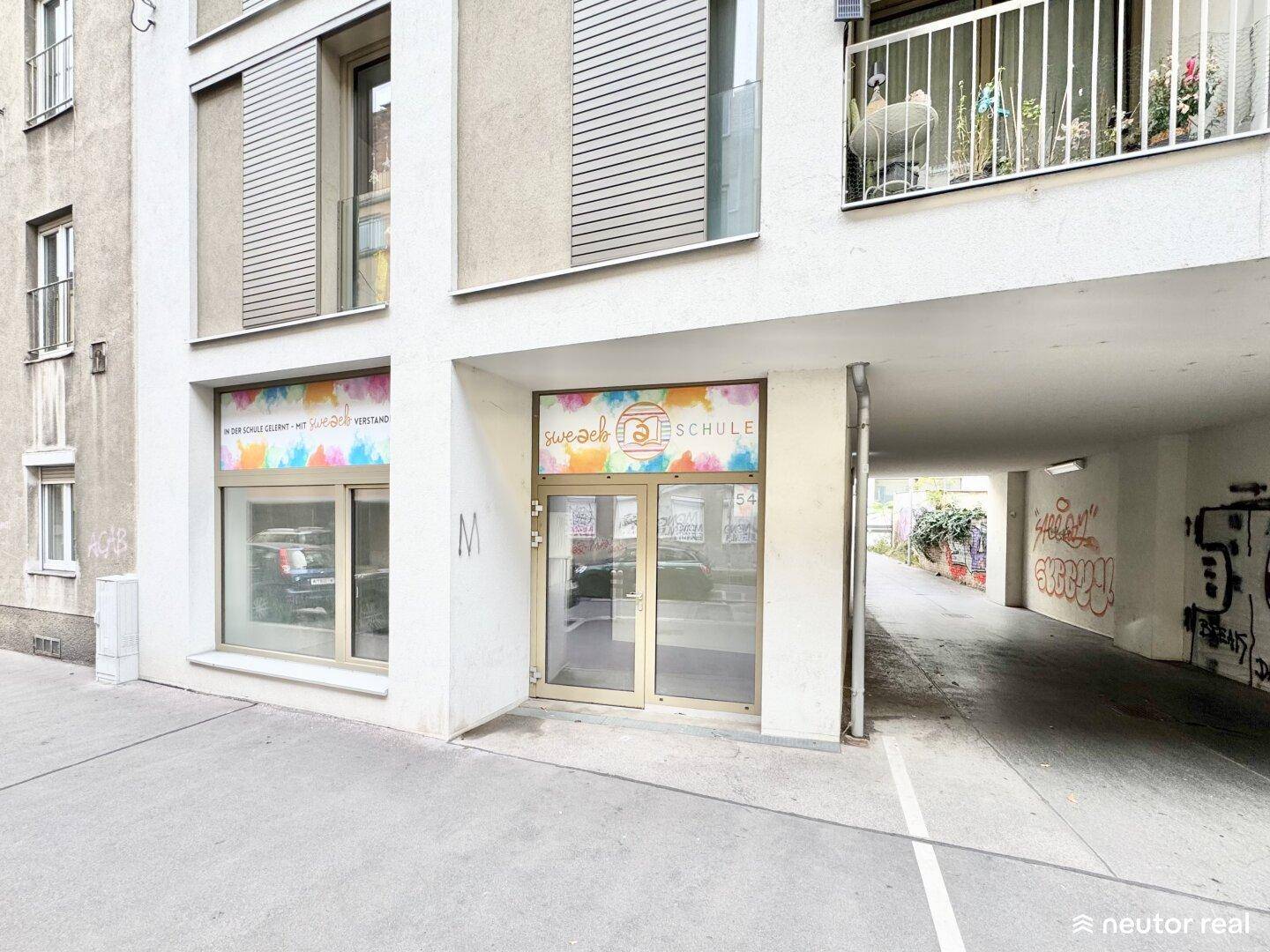 Moderne Gebäudefassade mit farbenfroher Beschilderung im Erdgeschoss und Balkonen darüber.