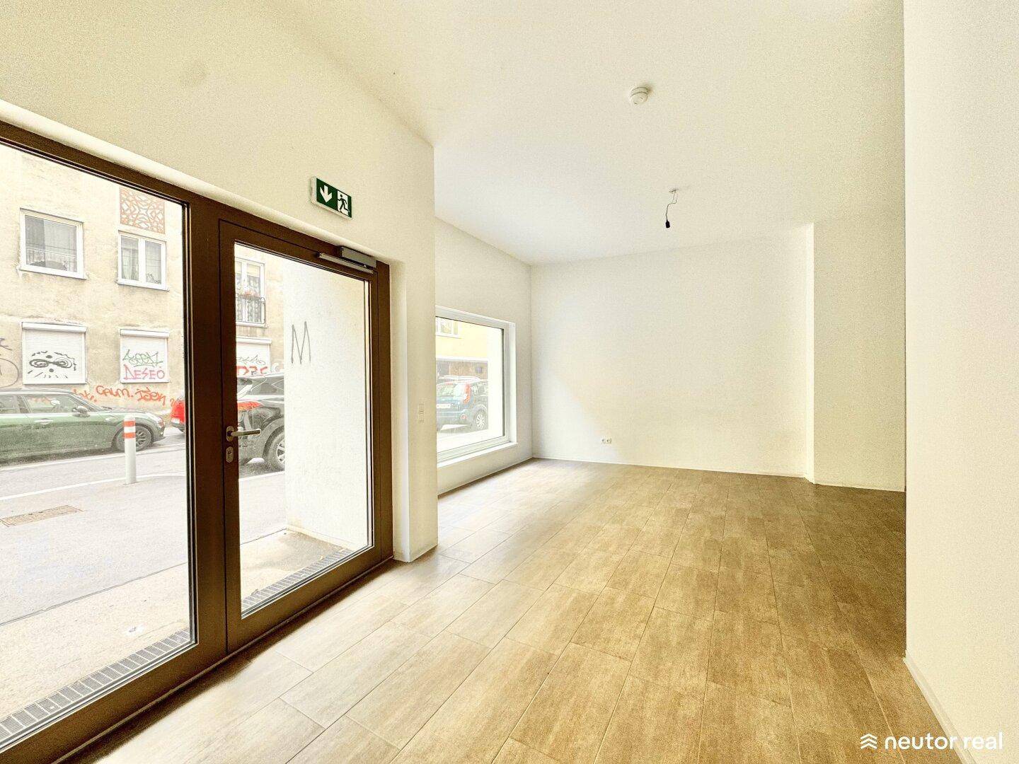 Geräumiger, heller Innenraum mit Fliesenboden, großen Fenstern und direktem Zugang zur Straße.