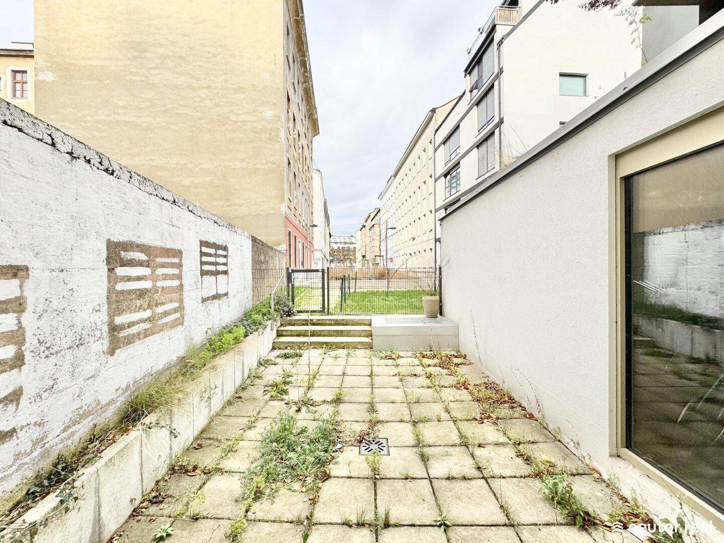 Hinterhof mit Pflastersteinen und einem Tor, umgeben von Gebäuden in städtischer Umgebung.