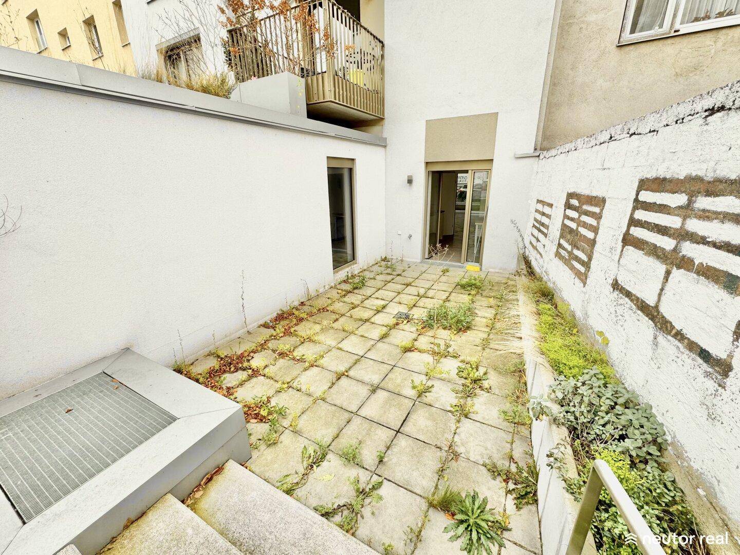 Gepflasterte Terrasse mit Treppenzugang und Blick auf die umliegenden Gebäude.
