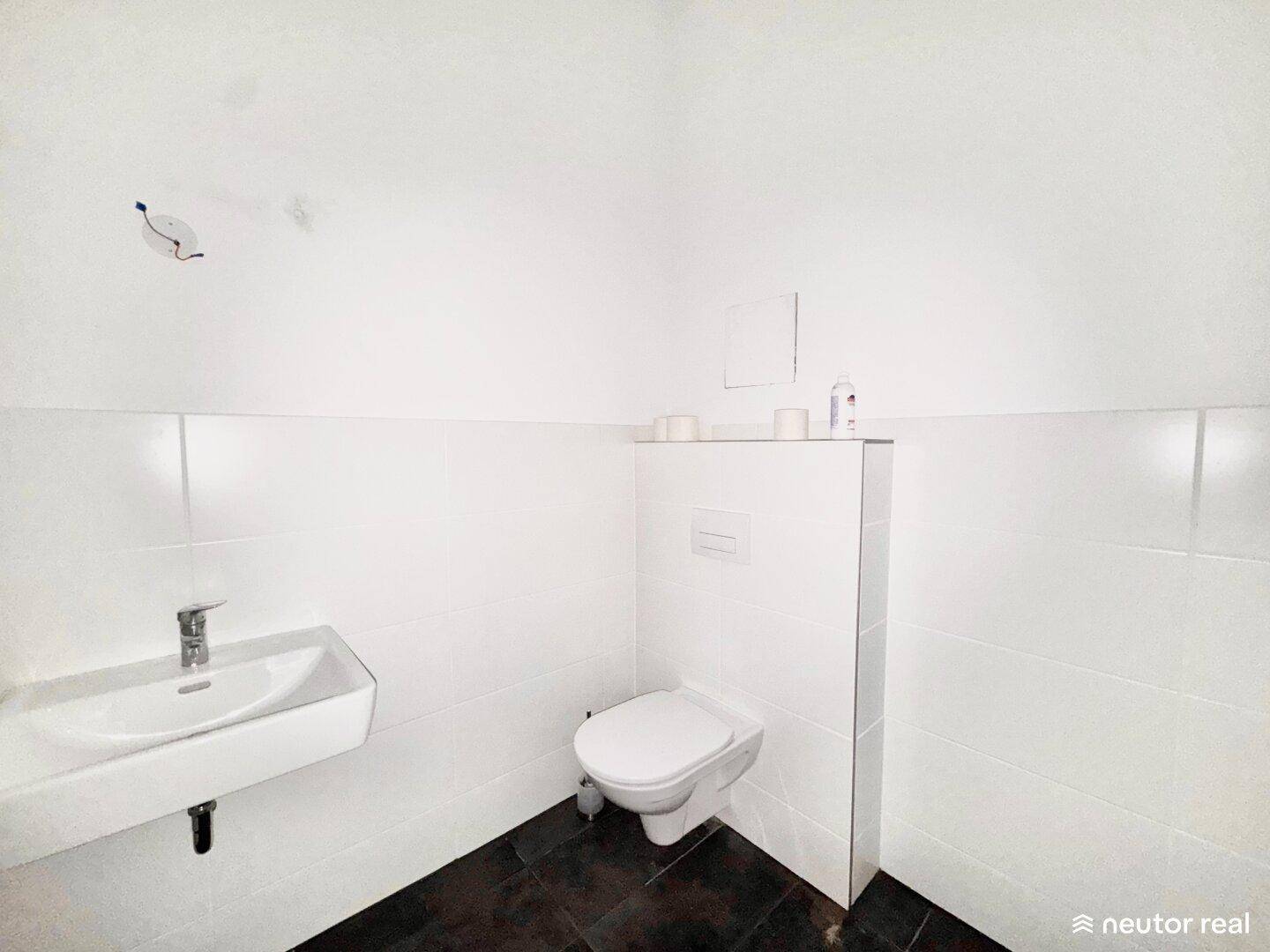 Modernes Gäste-WC mit wandhängender Toilette, kleinem Waschbecken und dunklem Fliesenboden.