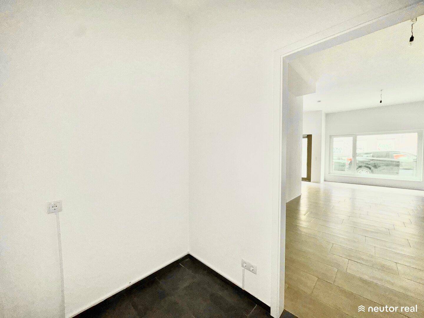 Kleiner Eckbereich mit dunklem Fliesenboden und Zugang zu einem größeren, hellen Raum.