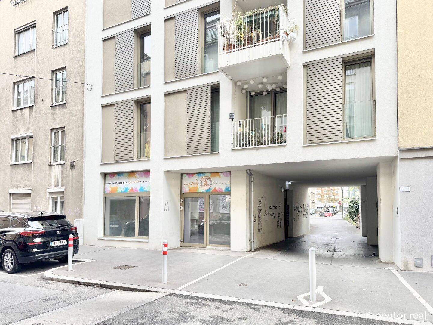 Moderne Gebäudefassade mit Balkonen, Fensterläden und einem Durchgang zur Straße.