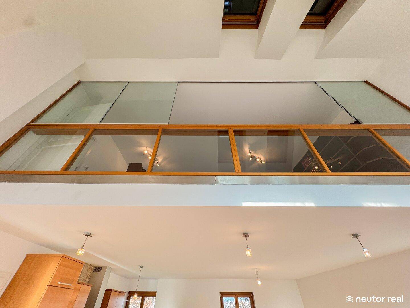 Hohe Decken und eine offene Galerie mit Holzrahmen und Glas, die den Raum lichtdurchflutet.