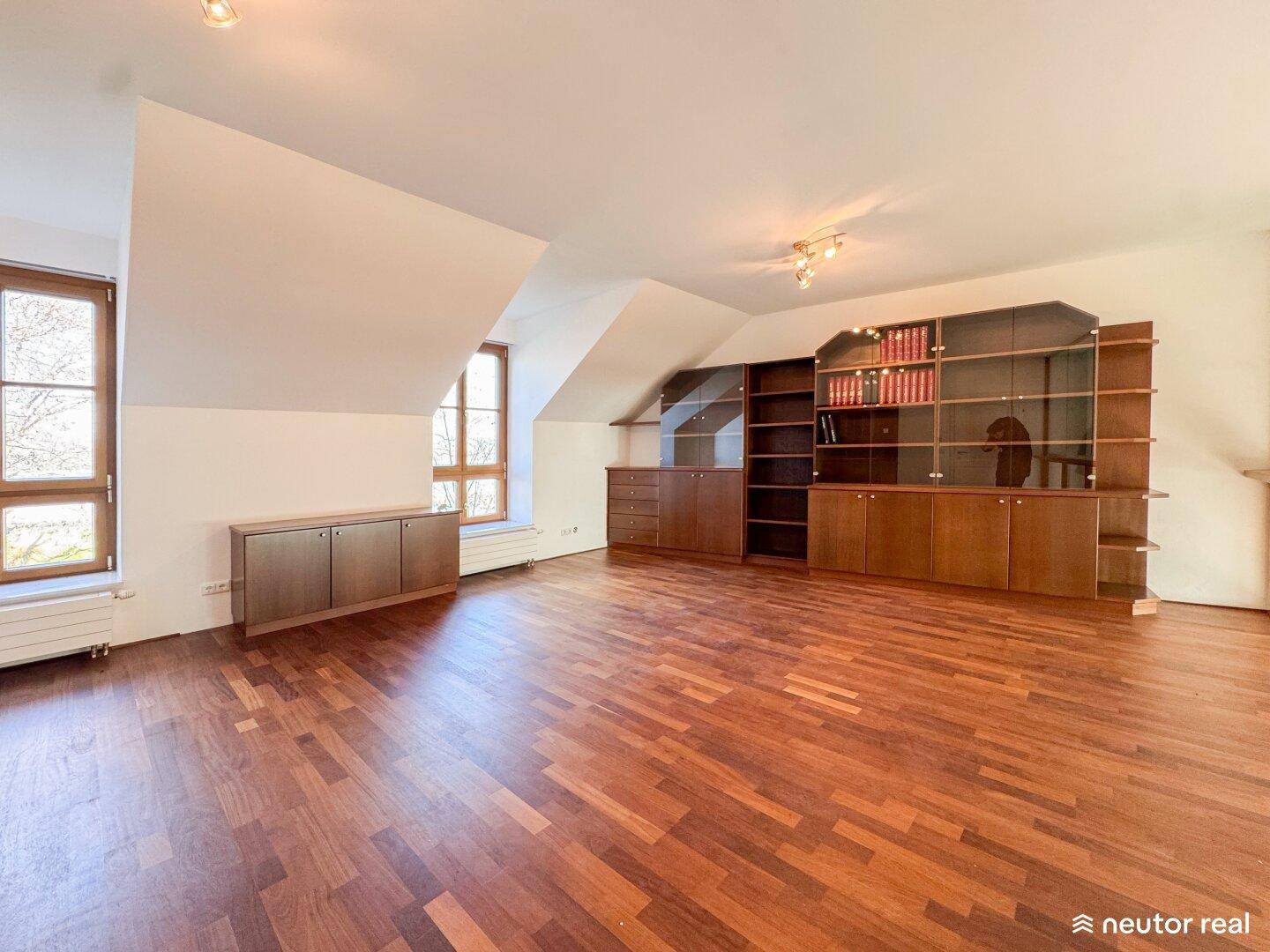 Geräumiges Zimmer mit Holzboden, Dachschrägen und eingebauten Bücherregalen.