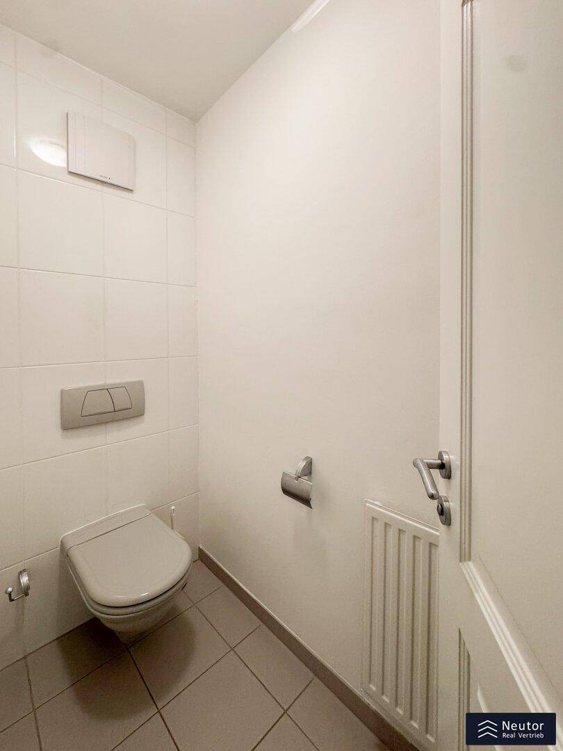 Modernes WC mit Wand-WC, Spülkasten und weißen Fliesen an Wänden und Boden.