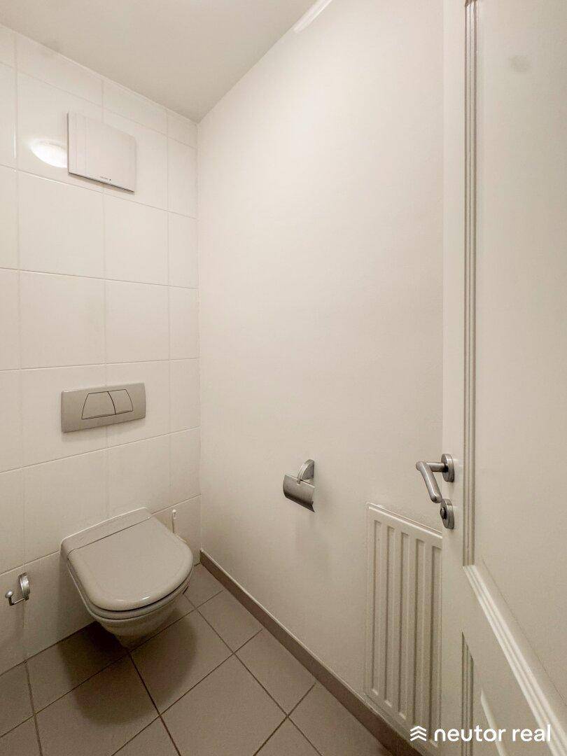 Modernes Gäste-WC mit wandhängender Toilette und weißen Fliesen, ausgestattet mit Heizkörper.