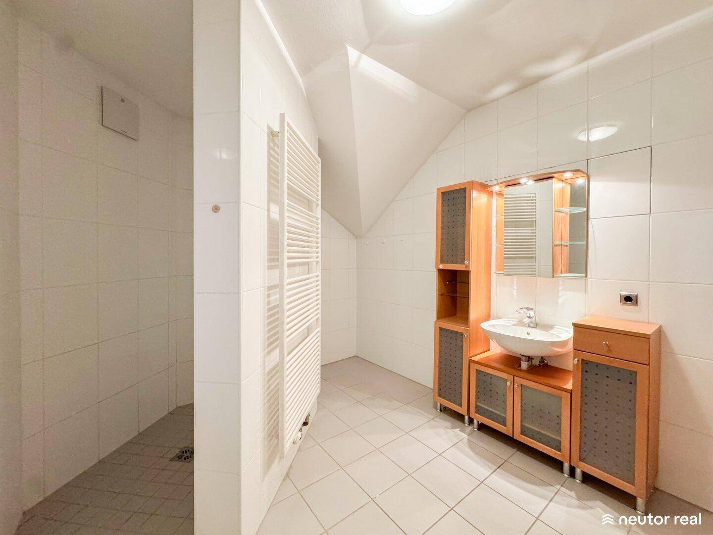 Gefliestes Badezimmer mit Dachschräge, Dusche und beheiztem Handtuchhalter.