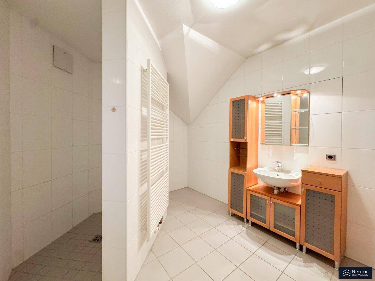 Helles Badezimmer im Dachgeschoss mit Dusche, Waschbecken und beheiztem Handtuchhalter.