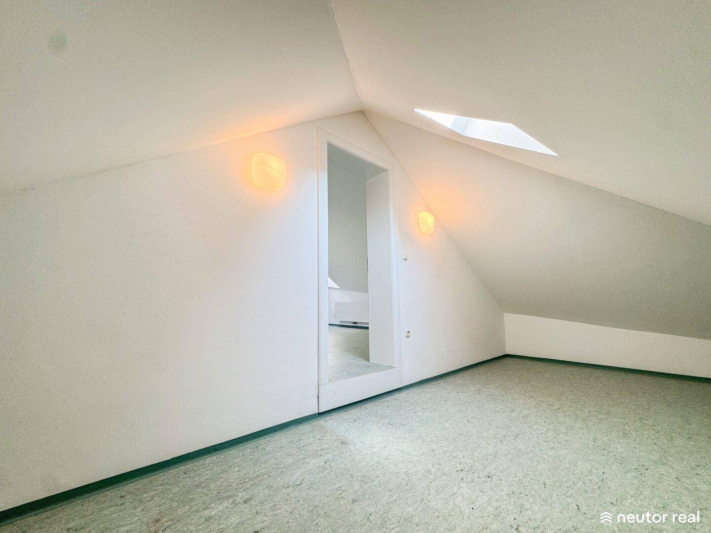 Dachzimmer mit Schrägen, Dachfenster und Zugang zu einem weiteren Raum.