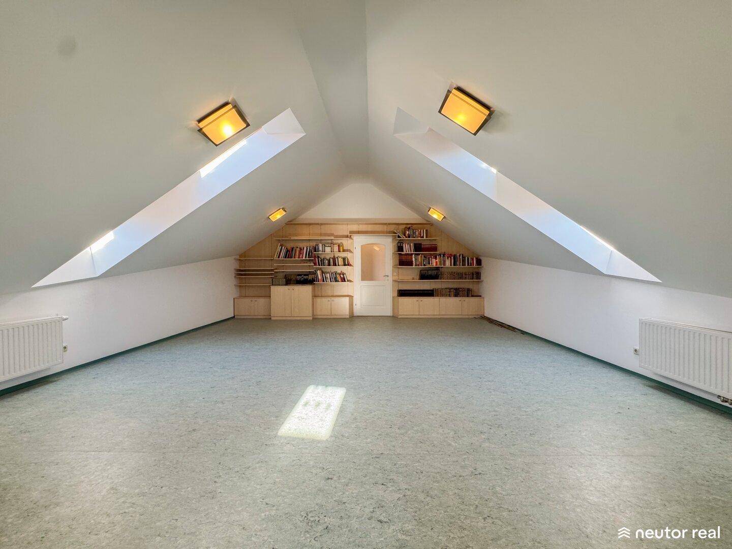 Helles Dachzimmer mit Schrägen, Dachfenstern und eingebauten Regalen.