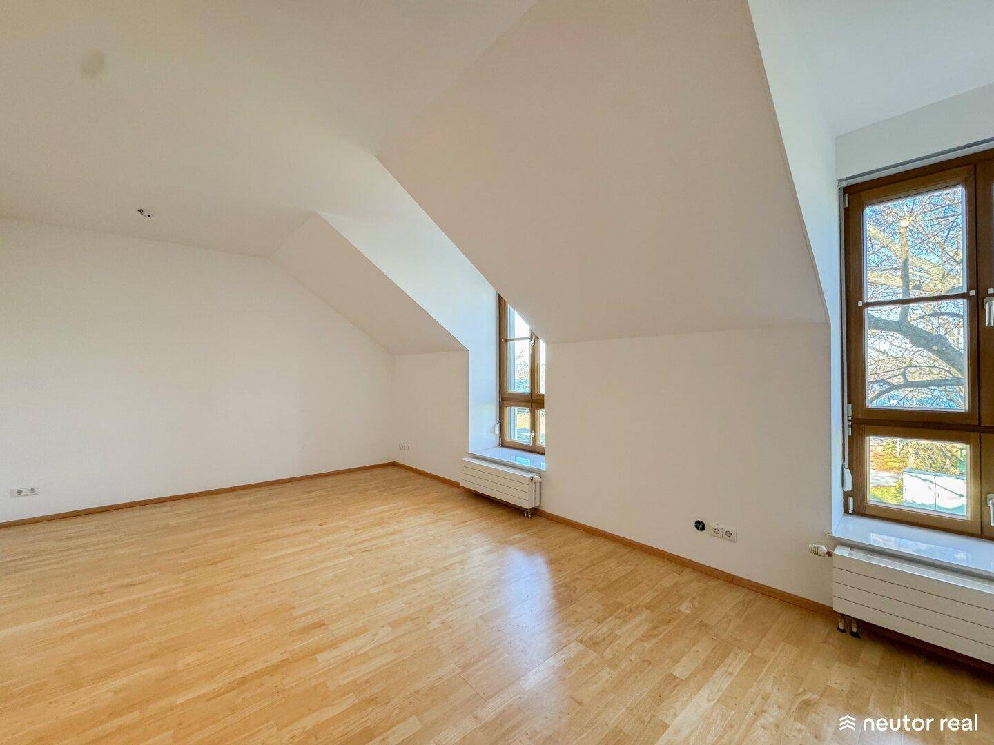 Geräumiges Zimmer mit Holzboden, Dachschrägen und großen Fenstern.